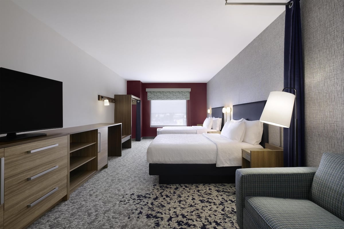 A hotel room with a bed, a TV, a desk, a chair, and a window.
