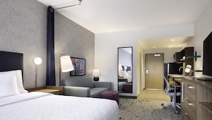 Une chambre d’hôtel avec un grand lit, un bureau, une chaise, une télévision et un miroir.