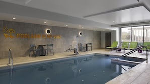 Un espace piscine intérieur moderne offrant une vue dégagée sur le bassin, des chaises longues et un mur orné de l’inscription « POOLSIDE IS MY VIBE ».