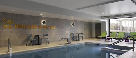 Un área de piscina interior moderna con vista despejada a la piscina, sillas de descanso y una pared con el texto 'POOLSIDE IS MY VIBE'.