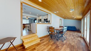 Un'ampia zona giorno con pavimento in legno, un tavolo da pranzo con sedie, un divano blu e una cucina sullo sfondo.
