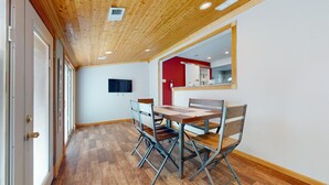 Una stanza con soffitto in legno, un tavolo da pranzo con quattro sedie, una TV a schermo piatto montata a parete e una parete di colore rosso.