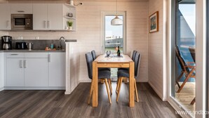 A modern kitchen with white cabinets, a microwave, and a coffee maker. There is a dining area with a wooden table and chairs. - Houseboat Harmony (Stralsund)
