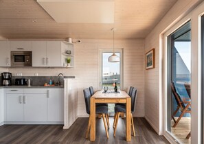 A modern kitchen with white cabinets, a microwave, and a coffee maker. There is a dining area with a wooden table and chairs. - Houseboat Harmony (Stralsund)