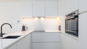 Una cocina compacta con armarios blancos, un grifo negro, un horno integrado y una cafetera sobre la encimera.