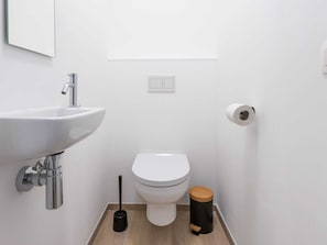 Un baño pequeño y moderno con lavamanos, inodoro y un cubo de basura blancos.