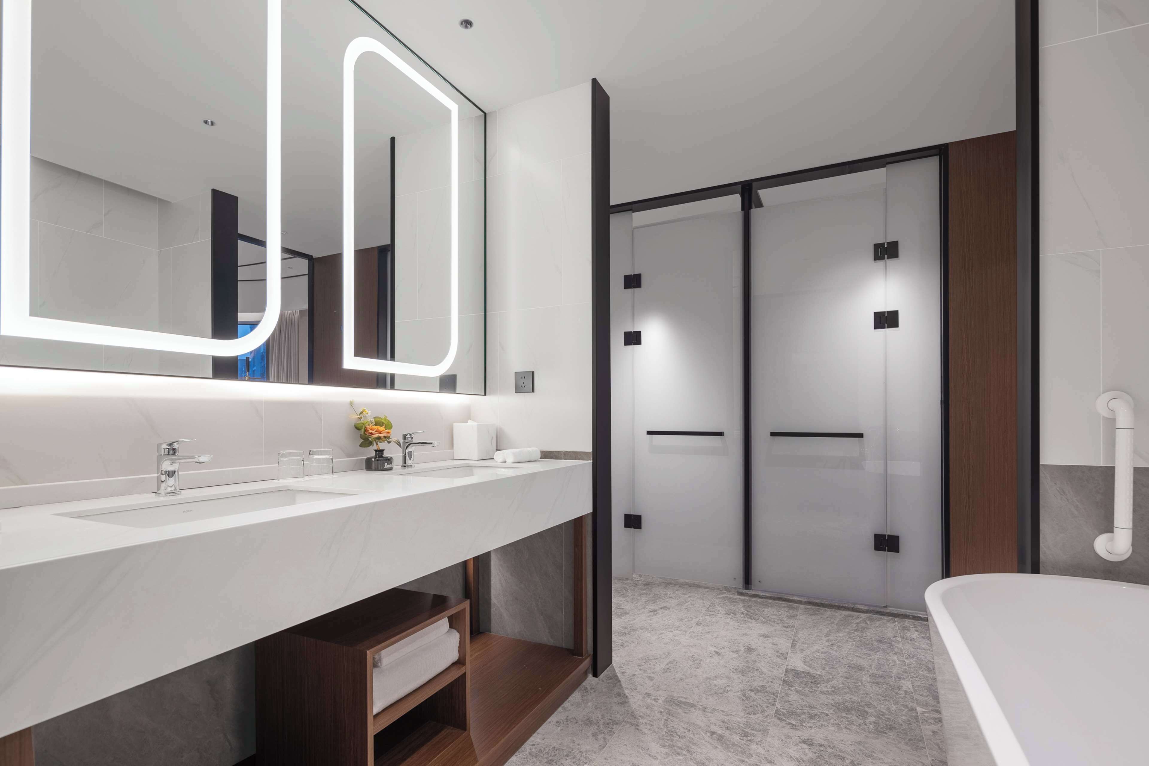 A modern bathroom with a large mirror, two sinks, a shower area, and a bathtub.