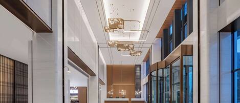 A spacious lobby with a modern design, featuring a reception desk, seating areas, and large windows.