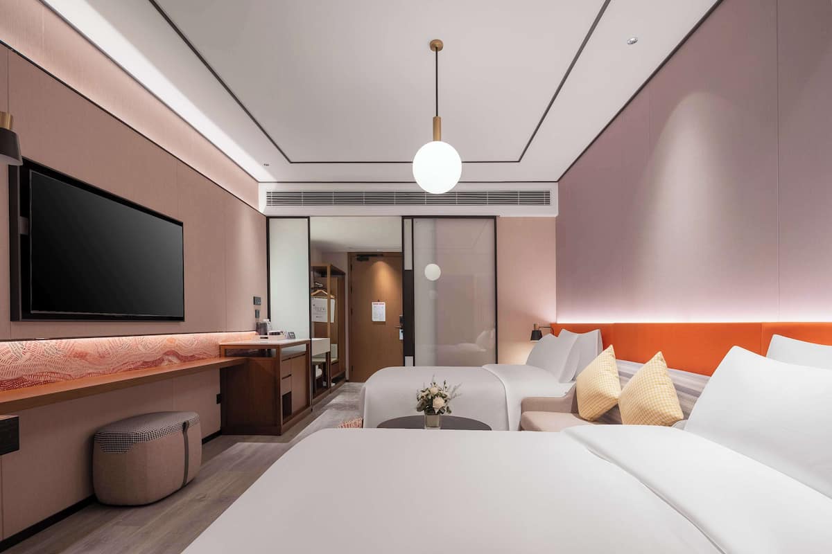 A modern hotel room with a large bed, a desk, a flat-screen TV, and a seating area with a sofa.