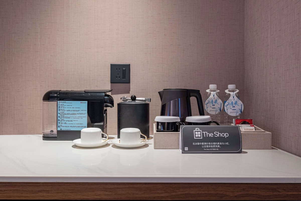 A hotel room's breakfast setup with a coffee maker, tea kettle, cups, and a sign reading "The Shop".