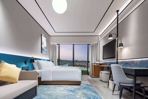 A modern hotel room with a large bed, a desk, a chair, a TV, and a view of a cityscape through large windows. - Hilton Garden Inn Yichang Yiling (Yichang)