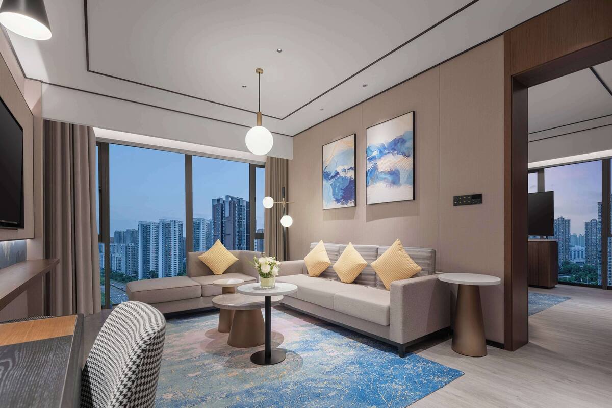 A modern hotel room with a large sofa, a coffee table, and a TV.