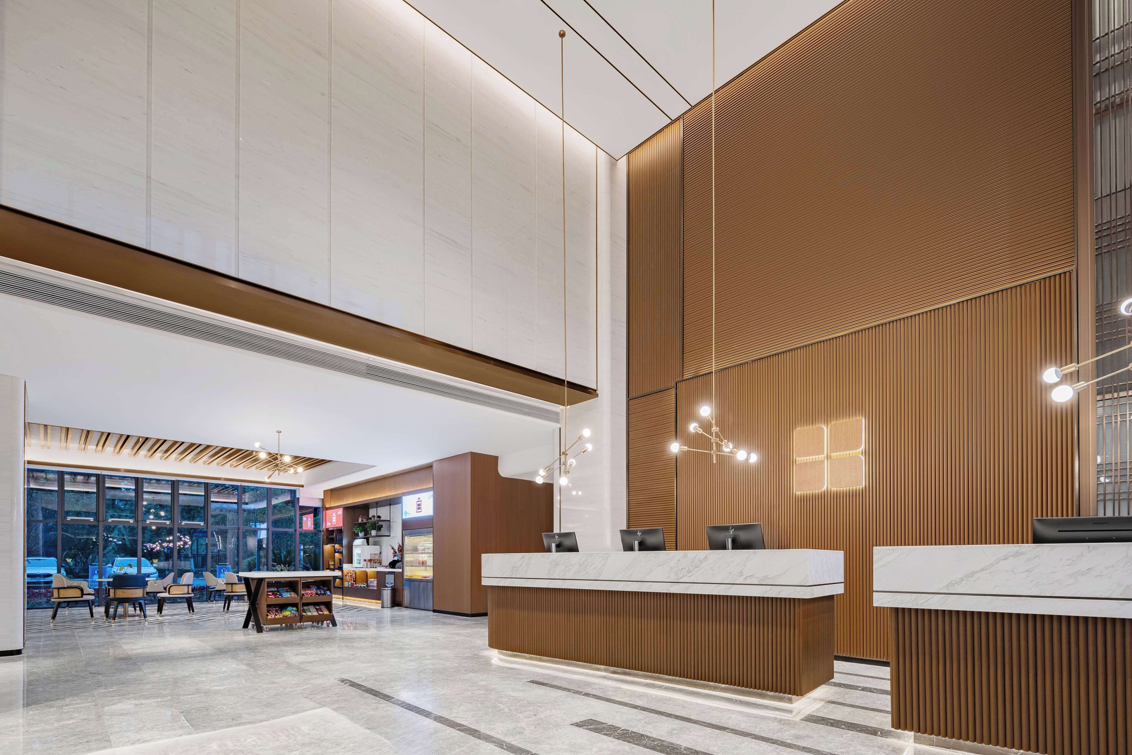 A modern hotel lobby with a reception desk, seating area, and large windows offering a view of the cityscape.