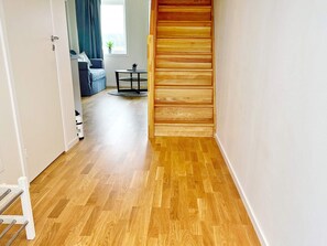 A hallway with wooden flooring, a staircase, and a view into a living area with a sofa and a small table. - 5 Person Holiday Home in Munso (Munsö)