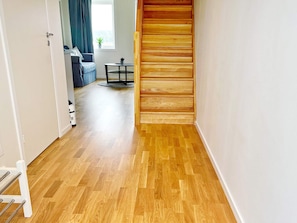 Un couloir doté d’un plancher en bois, d’une porte blanche et d’un escalier avec des marches en bois.