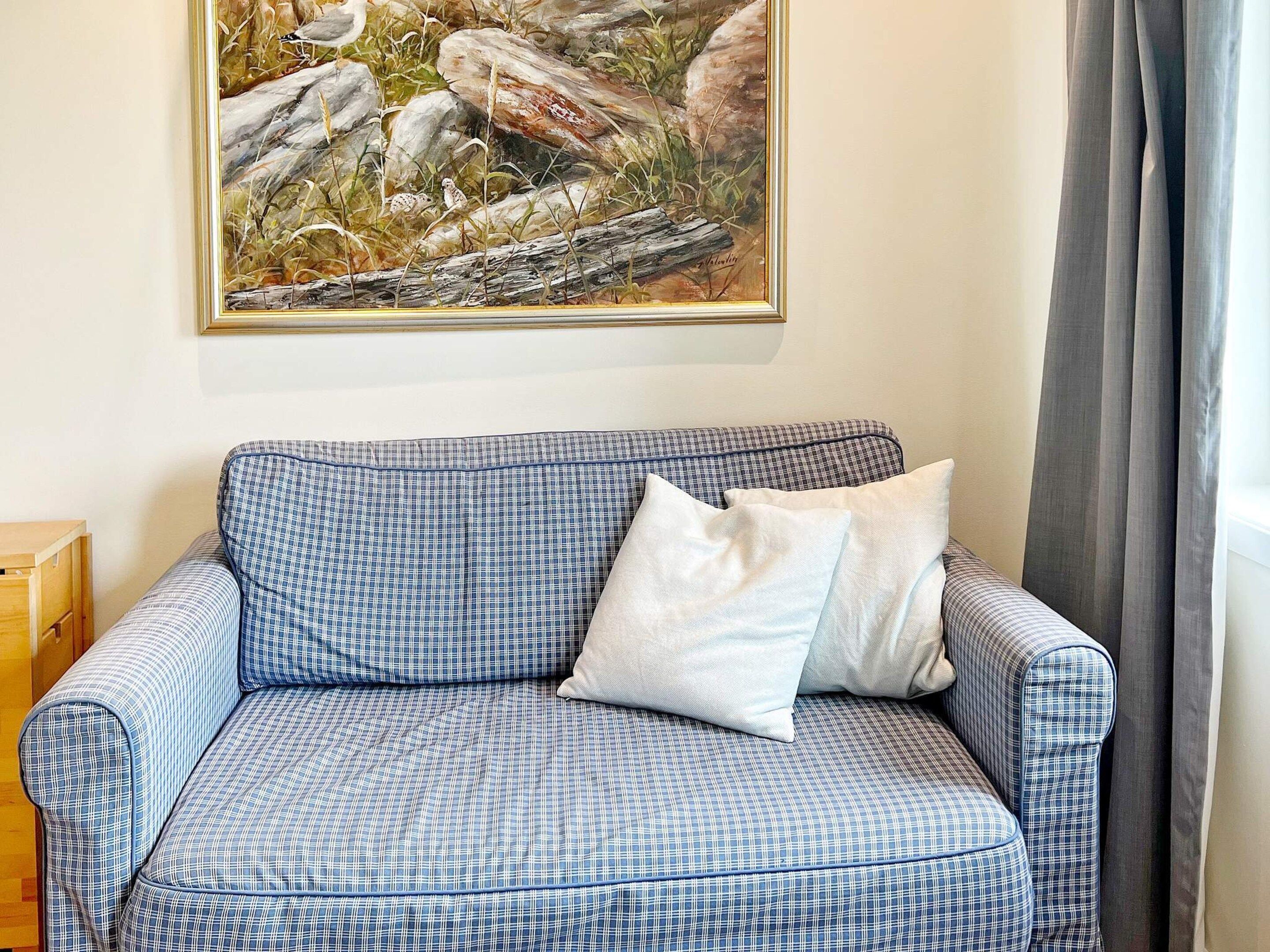Un canapé à carreaux avec un coussin, un tableau accroché au mur et une fenêtre avec des rideaux.