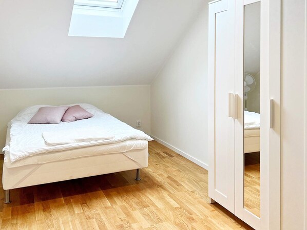 A bedroom with a bed, a skylight, wooden flooring, and a wardrobe.