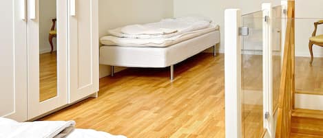 A bedroom with a single bed, wooden flooring, and a glass door leading to another room.