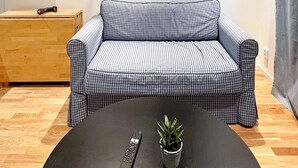A checkered sofa in a room with a wooden floor, a small table with a remote control and a potted plant, and a painting on the wall. - 5 Person Holiday Home in Munso (Munsö)