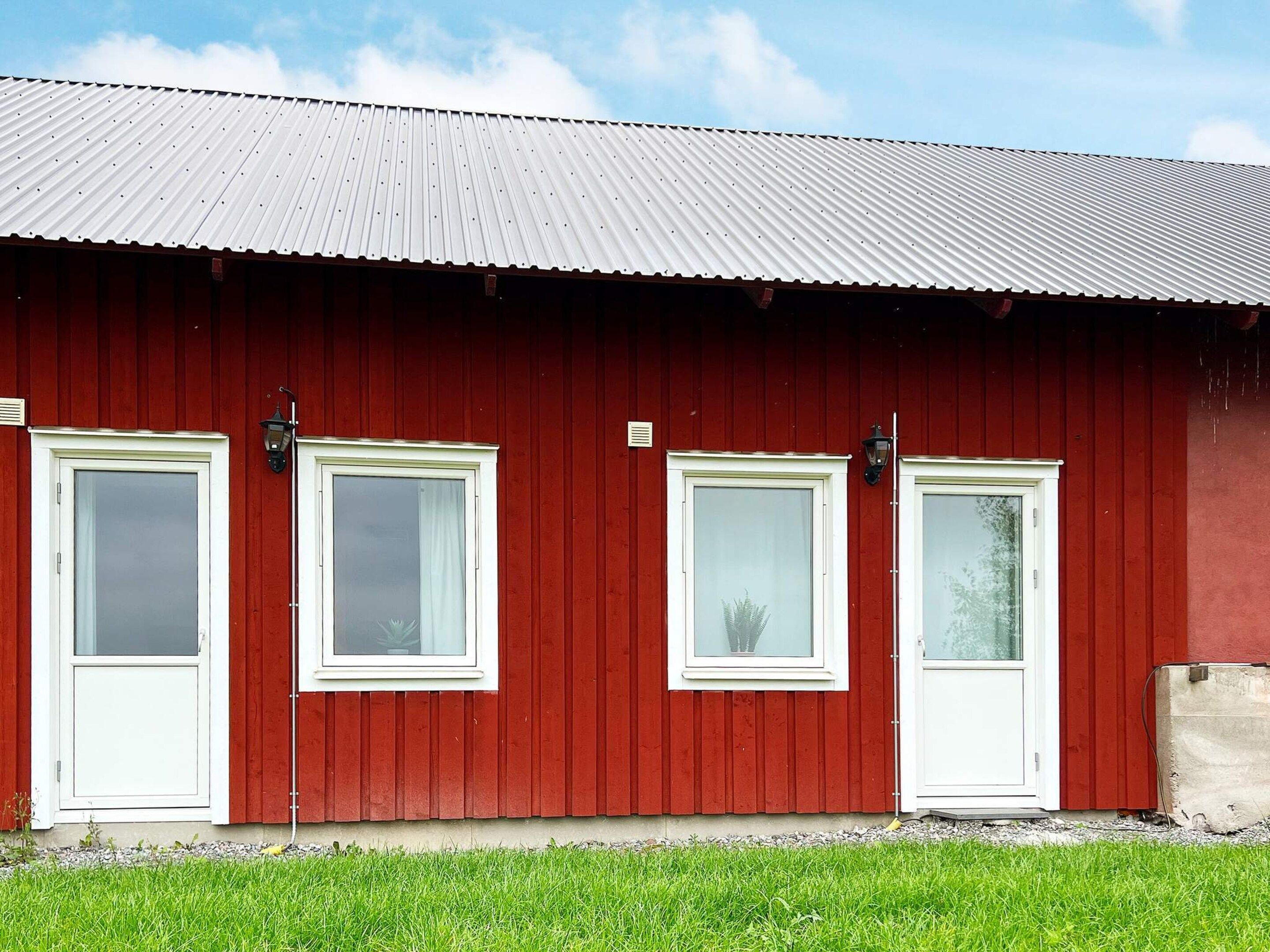 A red barn with four white-framed windows and a metal roof.