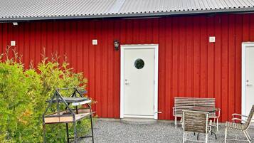 A red building with a white door and a small window. There is a bench and a table outside.