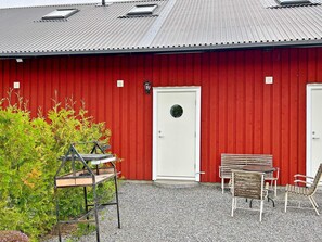 A red building with a white door and a small window. There is a bench and a table outside. - 5 Person Holiday Home in Munso (Munsö)