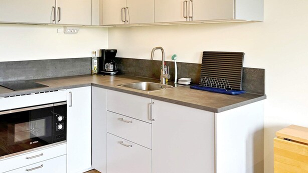 A modern kitchen with white cabinets, a Bosch oven, a coffee maker, and a sink with a faucet. - 5 Person Holiday Home in Munso (Munsö)
