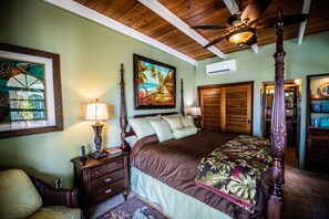 A bedroom with a four-poster bed, a nightstand with a lamp, a wooden ceiling, and a painting of a beach scene. - Villa Romance Free Concierge services (Cruz Bay)