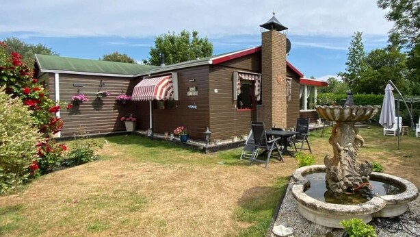 Una casa con techo rojo, chimenea y un patio con mesa y sillas.