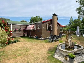 A house with a red roof, a chimney, and a patio area with a table and chairs. - Huijsmansverhuur Type C Comfort Plus Prinsenhof 79 (Ouddorp)