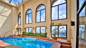 An indoor swimming pool with arched windows and city views. - HOTEL FARIA LIMA, LUXUOSO ALTO PADRÃO (São Paulo)