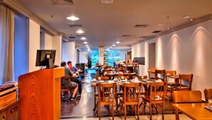 A restaurant with wooden tables and chairs, a counter with a coffee machine, and a view of the outdoors through large windows. - HOTEL FARIA LIMA, LUXUOSO ALTO PADRÃO (São Paulo)