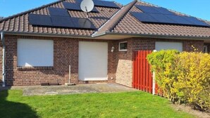 Une maison de plain-pied en briques, avec un toit en pente, des panneaux solaires, une clôture rouge et une pelouse bien entretenue.