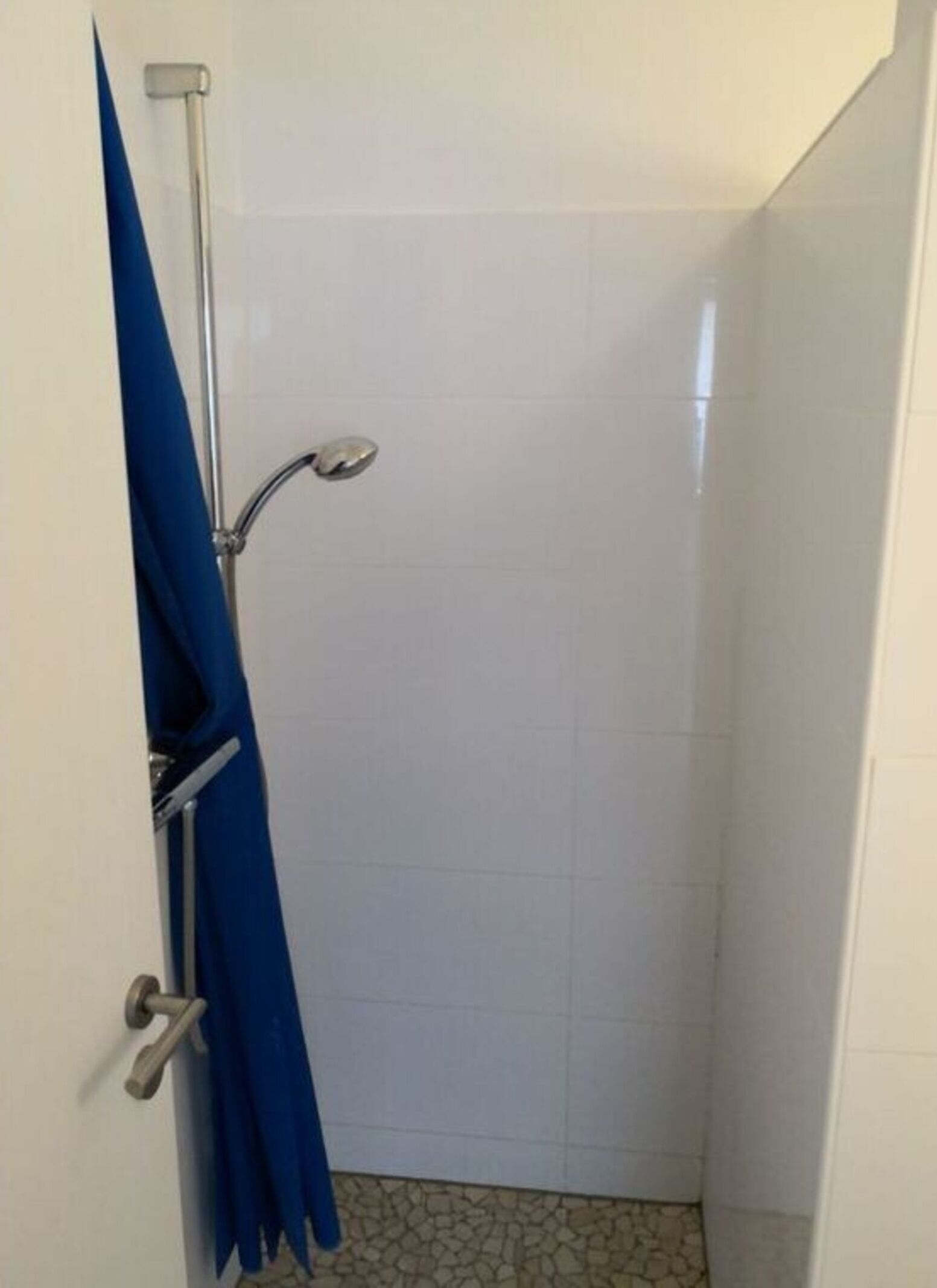 A small, enclosed shower area with white tiled walls and a tiled floor.