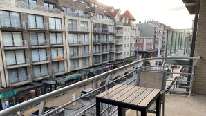 Un balcone con tavolo e sedie, affacciato su una strada con auto e un edificio con diversi balconi.