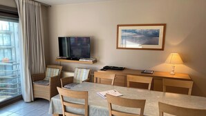 Una camera d'albergo con un tavolo, sedie, una televisione, una lampada e un quadro appeso al muro.