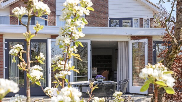Een modern huis met twee verdiepingen, een terras, een eettafel en stoelen.