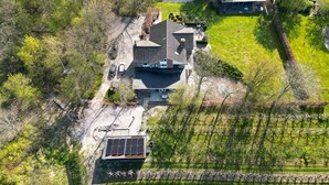 Luchtbeeld van een huis met een zonnepaneel, omringd door bomen en een kleine tuin.