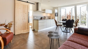 Een moderne keuken met een schuifdeur, een eethoek met een tafel en stoelen, en een woonkamer met een bank en een kleine tafel.