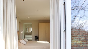 Een slaapkamer met een bed, nachtkastje, spiegel en uitzicht op een bakstenen muur.