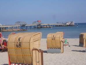 Wicker beach chairs with numbers on them, a pier in the background, and a clear sky. - My Holiday Home Comfortable Holiday Residence (Kellenhusen)