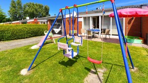 A swing set in a grassy area with a building in the background. - Holiday Home Weisse Robbe (Esens)