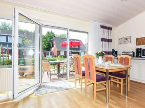 A dining area with a table and chairs, a kitchen area with appliances, and a view of the outside through a glass door. - Holiday Home Weisse Robbe (Esens)