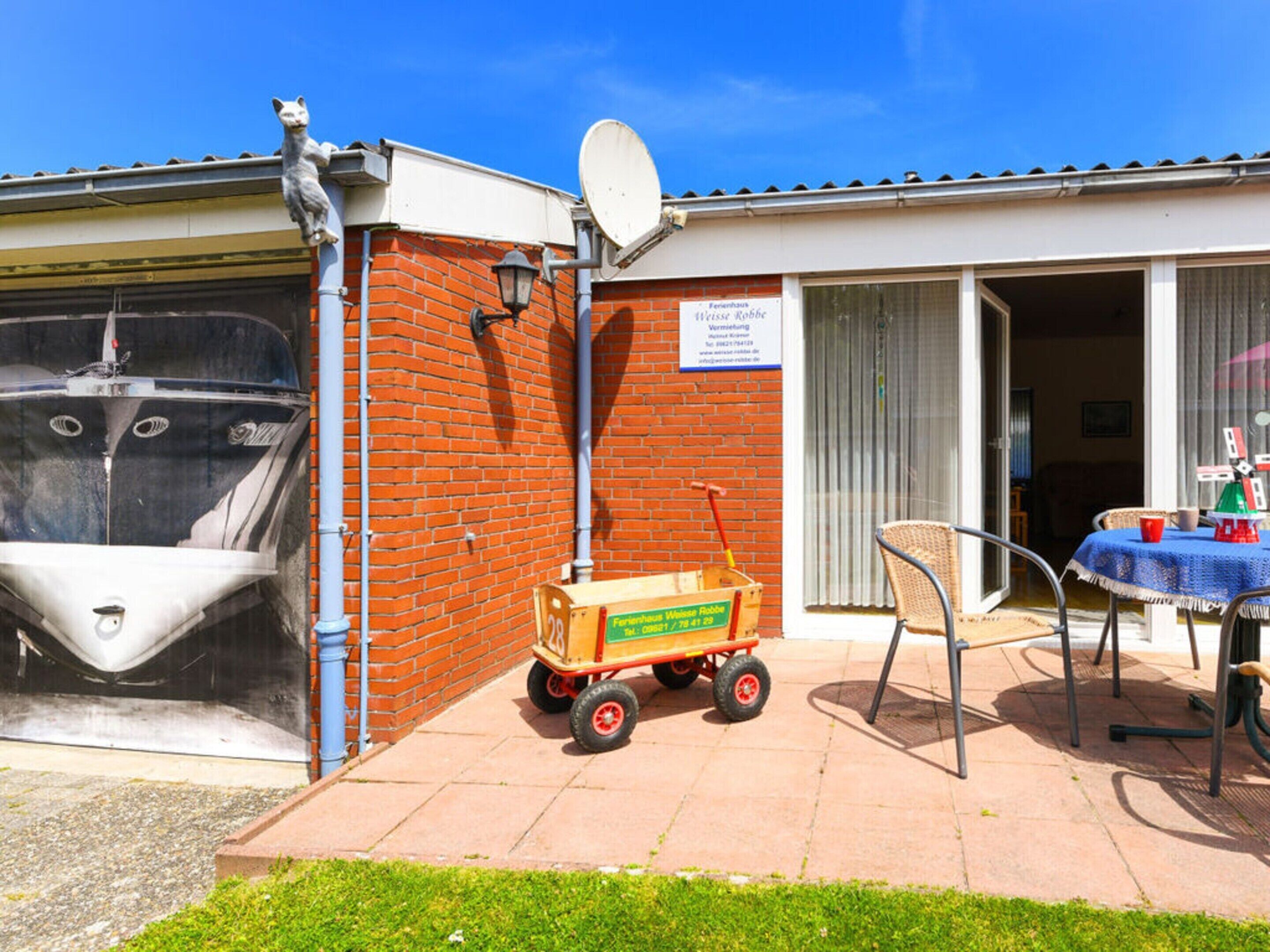 A building with a satellite dish, a brick wall, a small cart, and a table with chairs outside.