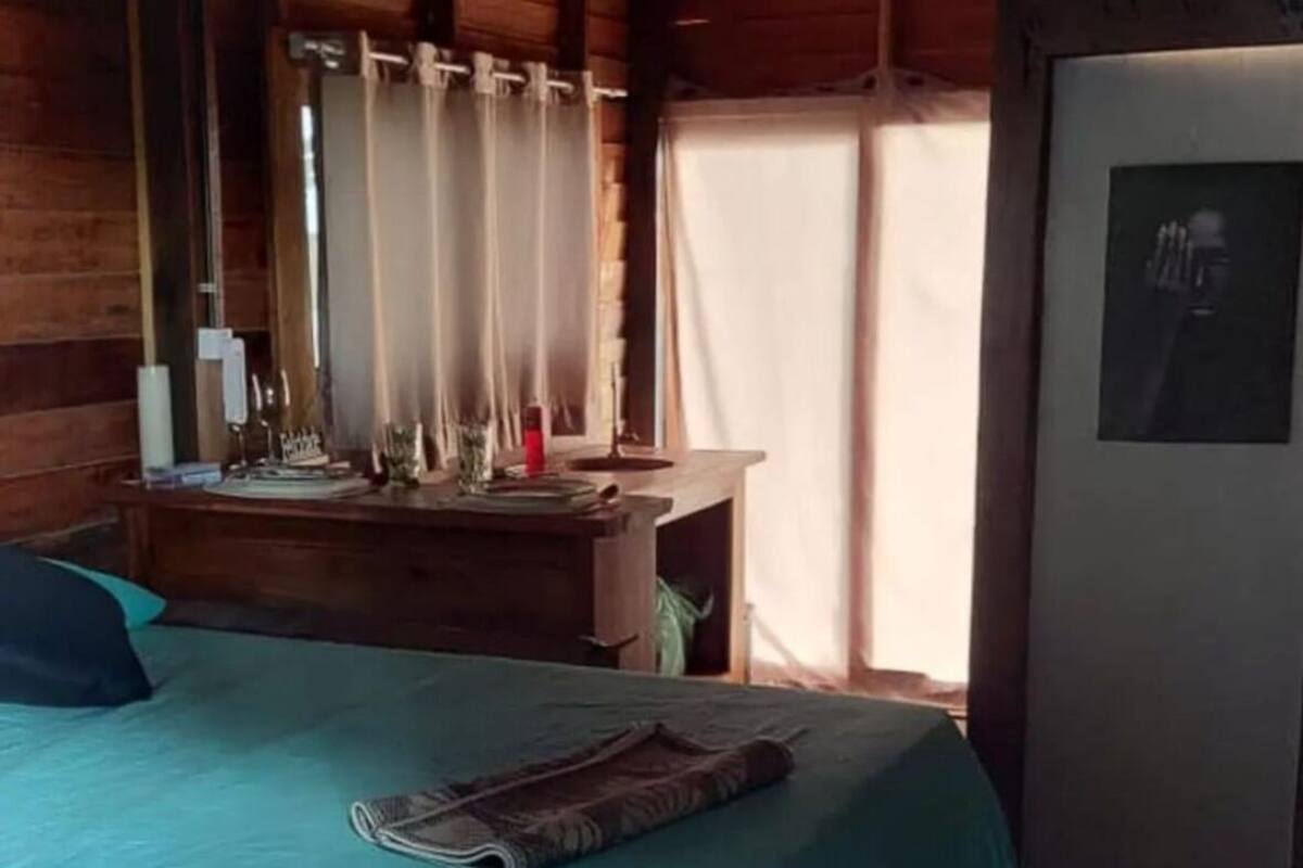A wooden cabin room with a bed, a desk, and a window with curtains.