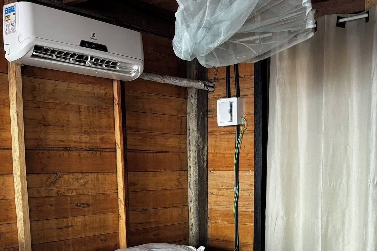 A wooden cabin room with a bed, a ceiling fan, and an air conditioning unit.