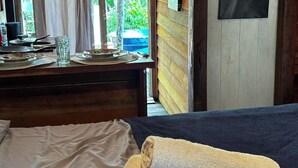 A wooden cabin room with a bed, a table with breakfast items, and a window with curtains. - Chale das Torres (Belém)