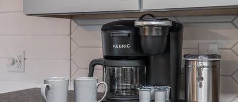 Una cafetera Keurig con una jarra de café, dos tazas y un recipiente de acero inoxidable para té sobre una encimera de cocina.