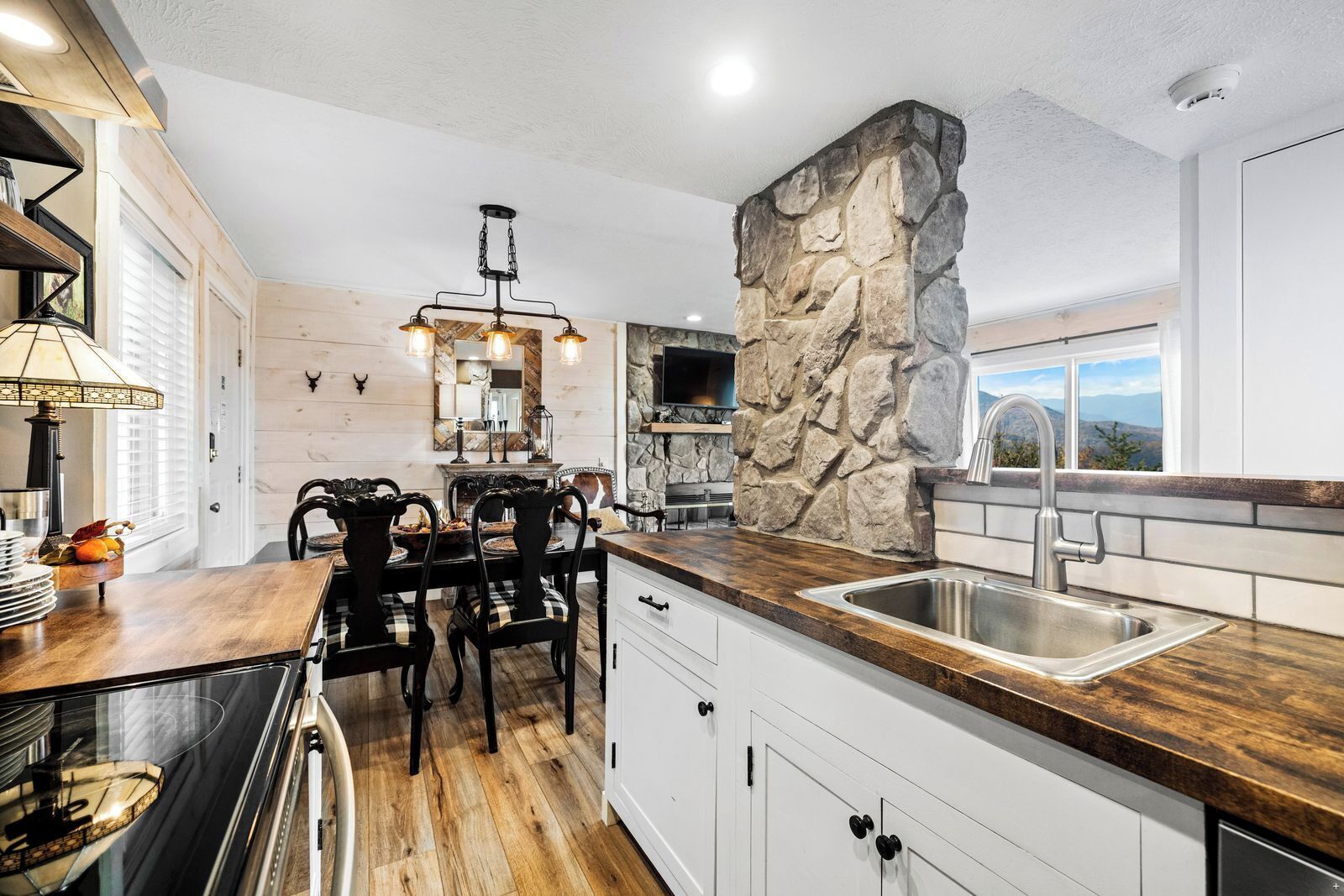 A kitchen with a stone accent wall, wooden countertops, and a dining area with a chandelier.
