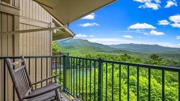 A wooden deck with a green railing overlooking a mountainous landscape.